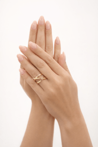 Modern tasarımlı VIP geometrik gold yüzük, nude pembe manikürlü kadın eli üzerinde açık stüdyo arka planında.